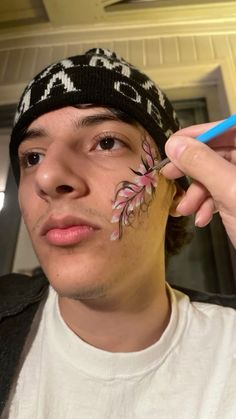 a young man is painting his face with flowers on the side of his head and holding a blue marker