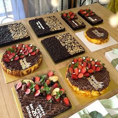 six cakes with chocolate frosting and strawberries on them sitting on top of a table