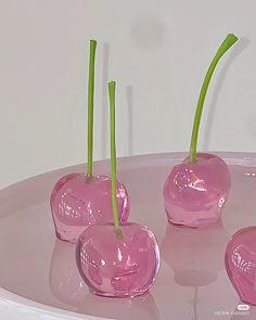 three pink vases with green stems sticking out of them on a white table top