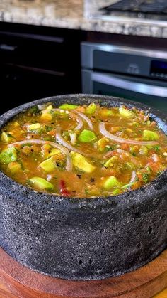 a bowl of vegetable soup sitting on top of a wooden table next to an oven