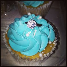 two cupcakes with blue frosting and a diamond ring on top are sitting on a plate