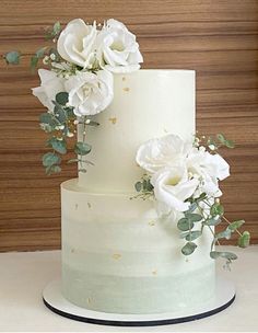 a three tiered cake with white flowers and greenery