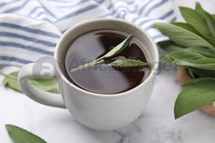 a cup filled with liquid next to green leaves on top of a white table cloth