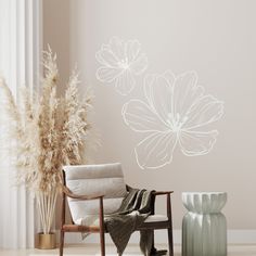 a chair sitting in front of a wall with white flowers on it and a vase next to it