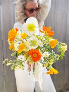 a woman in white pants holding a bouquet of flowers with her hands behind her back