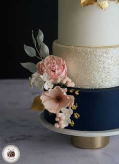 three tiered wedding cake with flowers on top and gold leaf decoration around the edges