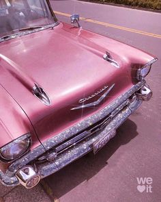 an old pink car is parked on the side of the road