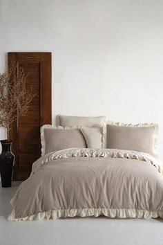 the bed is made up with ruffled linens and pillows, along with a wooden headboard