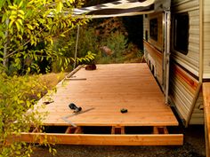 an rv is parked in the woods with its awning open and it's wooden deck