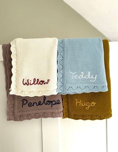 three towels hanging on the wall with name written on them and two folded ones in different colors