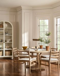 a dining room table surrounded by chairs in front of two windows with open shelving