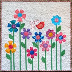 a quilted wall hanging with colorful flowers and a bird on the flower stems in it