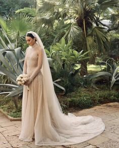 a woman in a wedding dress standing on a brick walkway with palm trees behind her