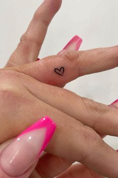 two fingers with hearts tattooed on them, one is pink and the other is black