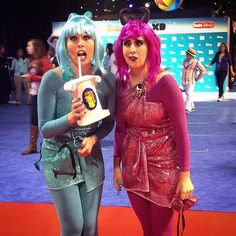 two women dressed up in costumes posing for the camera at an indoor convention or show