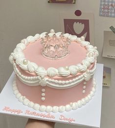 a pink and white birthday cake with a tiara on top is being held by a person