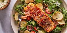 a white plate topped with salmon and salad next to a bowl filled with bread slices