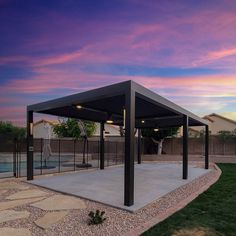 a covered patio area next to a swimming pool at dusk with pink clouds in the sky