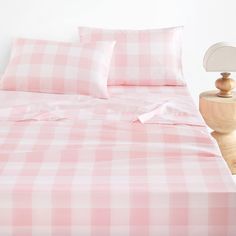 a bed with pink and white checkered sheets, pillows and a wooden night stand