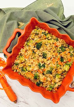 an orange dish filled with rice and broccoli on top of a white table