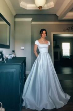 a woman in a white dress standing next to a dresser