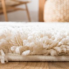 a fluffy white cat laying on top of a wooden floor next to a pillow and chair