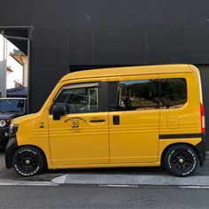 a yellow van parked on the side of a road next to a black car and building