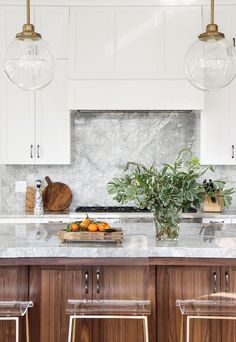 a kitchen with white cabinets and marble counter tops, two hanging lights above the island