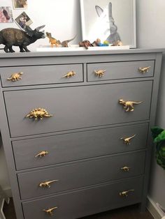 a gray dresser with gold handles and dinosaurs on it's knobs, in a child's bedroom