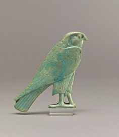 a small green bird figurine sitting on top of a white table next to a gray wall