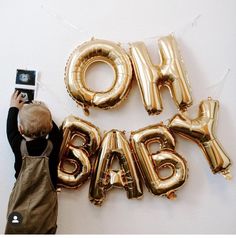 a young boy taking a photo with his cell phone next to balloons that spell out the word oh baby