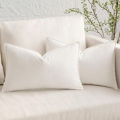 three white pillows sitting on top of a couch next to a vase with green plants