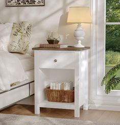 a white nightstand with a basket on it next to a bed