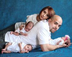 a man and woman are laying on a couch with their two babies in their arms