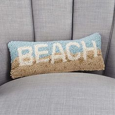 a pillow that says beach on the back of a gray chair with blue and gold pillows