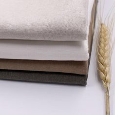 three different colors of fabric next to each other on a white surface with a stalk of wheat in the foreground