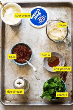 the ingredients to make this dish are displayed on a baking sheet, including sour cream, mayonnaise, cumin, chili powder and cilantro