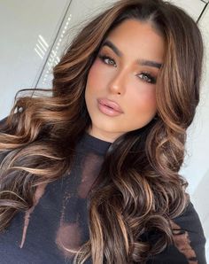 a woman with long brown hair wearing a black top and posing for the camera in front of an umbrella