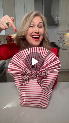 a woman holding up a red and white striped gift bag with a bow on it