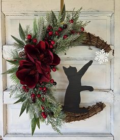 a christmas wreath hanging on the front door with a cat and poinsettis