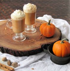 two pumpkins are sitting on a table next to some cups with whipped cream in them