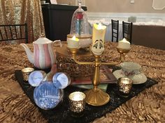 a table topped with tea cups and candles on top of a black cloth covered table