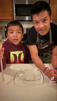 a man standing next to a little boy in front of a glass bowl on top of a counter