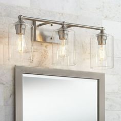 a bathroom vanity light with three clear glass jars on the wall above it and a mirror