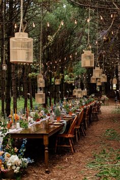 a long table with birdcages hanging from it's ceiling in the woods