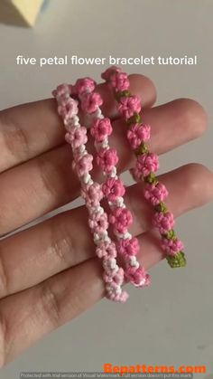 a hand is holding three pink and white flower bracelets