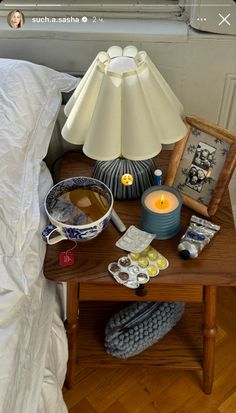 a table topped with a lamp and pictures next to a night stand on top of a bed