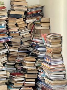 a large stack of books sitting on top of a wooden floor next to a white wall