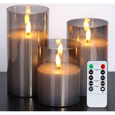 three lit candles sitting next to each other on a table with remote controls in front of them