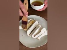 a person is holding a brush over some food on a plate with a cup of tea